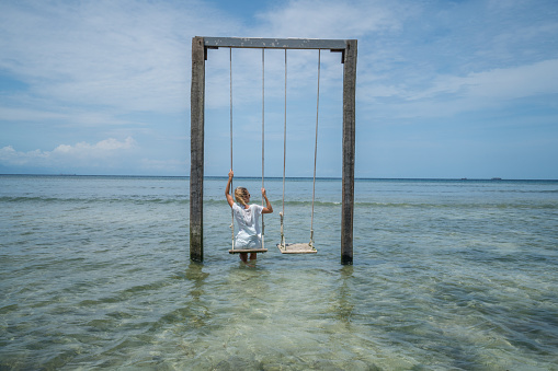 Young woman swinging over the sea, beautiful and idyllic landscape. People travel vacations concept.