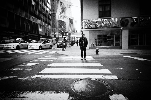 A rock fan crossing the street adjoining Lexington Avenue. He is in the center of the frame and walking nonchalantly across the road with yellow cabs on the left waiting at another crossing.
