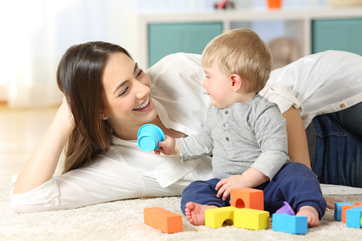 Joyful mother and baby playing with toys on a carpet at home