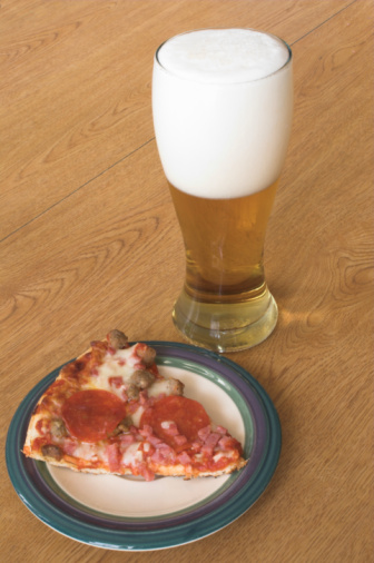 A slice of pizza and a beer in a pilsner glass.