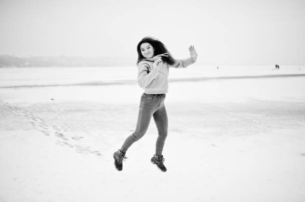 Funny jumping girl on frozen lake in winter day.