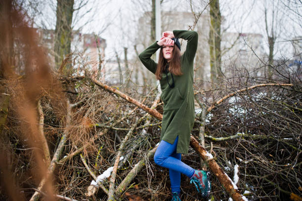Young girl wear on long green sweatshirt, jeans and black headwear at  branches of the pine tree in winter day.