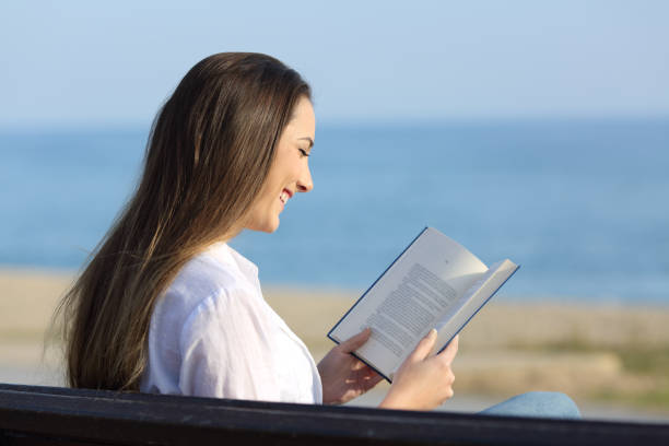 istock Woman reading a book sitting on a bench on the beach 912915146
