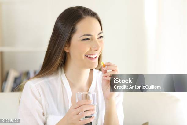 Photo libre de droit de Femme Heureuse Prendre Une Pilule De Vitamine Jaune À La Maison banque d'images et plus d'images libres de droit de Gélule