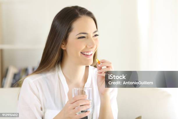 Happy Woman Taking A Vitamin Yellow Pill At Home Stock Photo - Download Image Now - Capsule - Medicine, Women, Vitamin