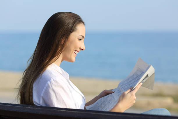 istock Woman reading a newspaper sitting on a bench on the beach 912915486