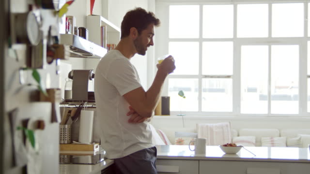 彼の台所に立っている間にオレンジジュースを飲んでいるハンサムな若者の4kビデオ映像