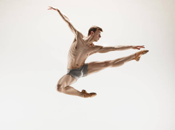Athletic ballet dancer in a perfect shape performing over the grey background