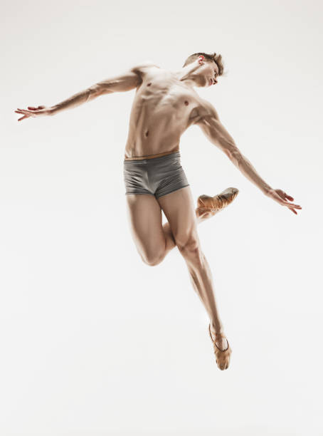 Athletic ballet dancer in a perfect shape performing over the grey background.