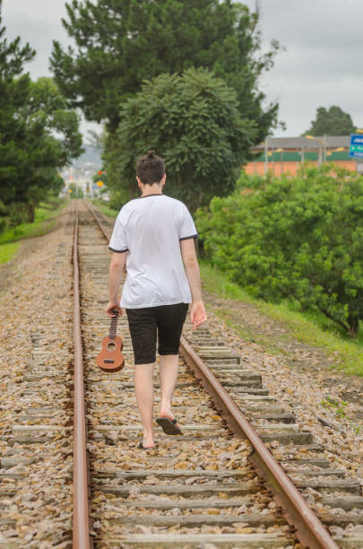 istock Man walking alone on train rail with his ukulele 912943612