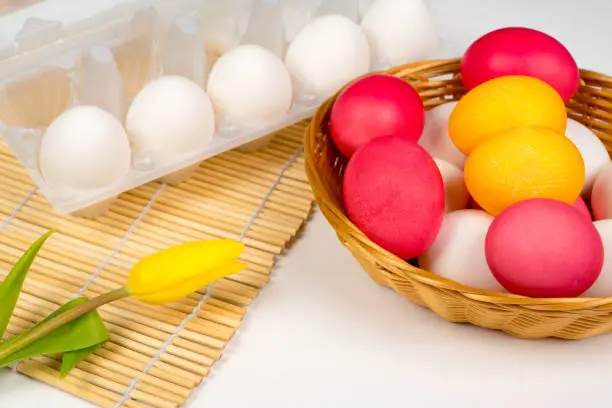 easter background, white and colored eggs in basket with yellow tulip over bamboo mat