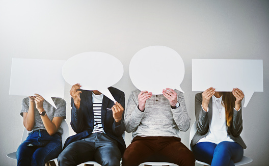 Shot of a diverse group of businesspeople holding up speech bubbles while they wait in line