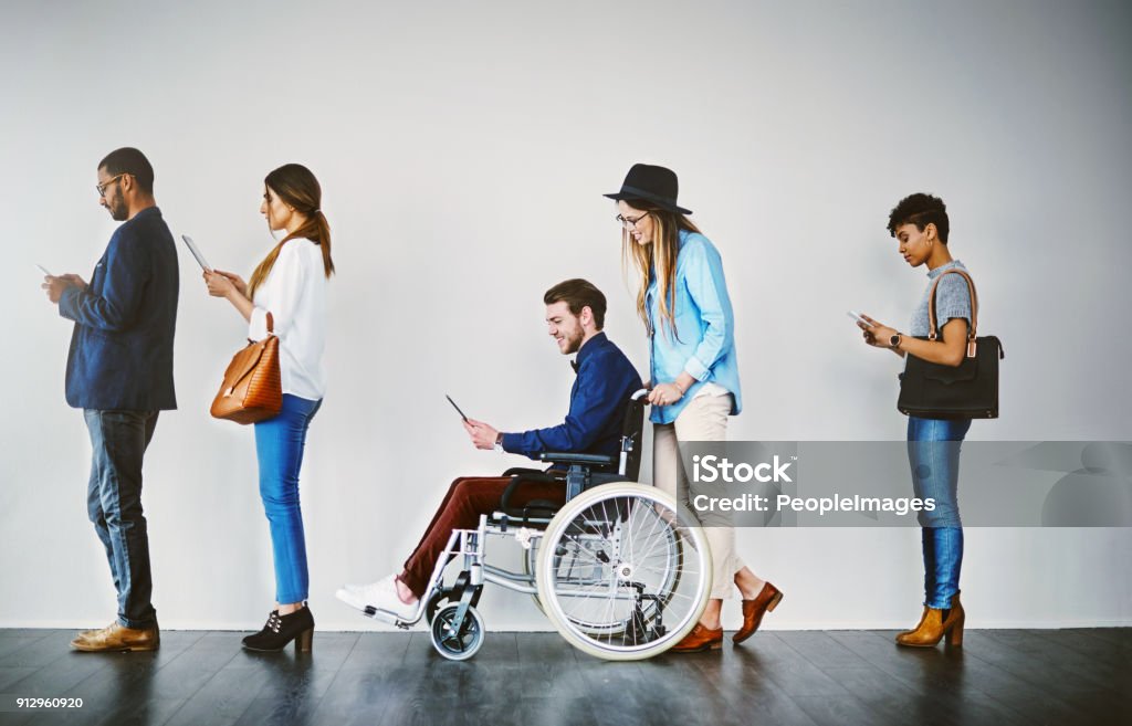 This interview is open to everyone Shot of a group of businesspeople using wireless technology while waiting in line Disability Stock Photo