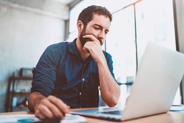 istock Young businessman working at sunny work place on laptop while sitting at the wooden table.Blurred background.Horizontal. 912962104