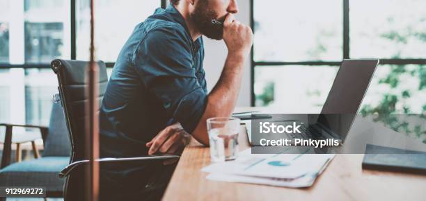 Young Pensive Coworker Working At Sunny Work Place Loft While Sitting At The Wooden Tableman Analyze Document On Laptop Displayblurred Backgroundhorizontal Wide Stock Photo - Download Image Now