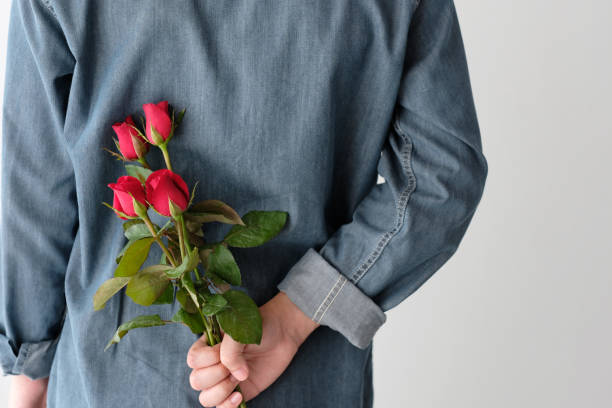 istock Valentine concept, Man holding red roses hiding on back on white background 912977826