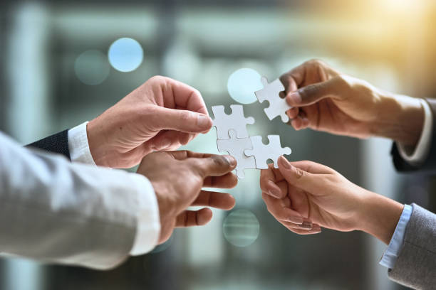 Teamwork, a sure solution to a business challenge Cropped shot of a group of businesspeople completing a puzzle together in a modern office coordination stock pictures, royalty-free photos & images