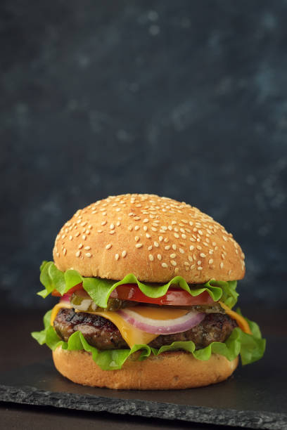 istock Homemade burger with beef, cheese, tomato, onion, salad on stone board. 912986584