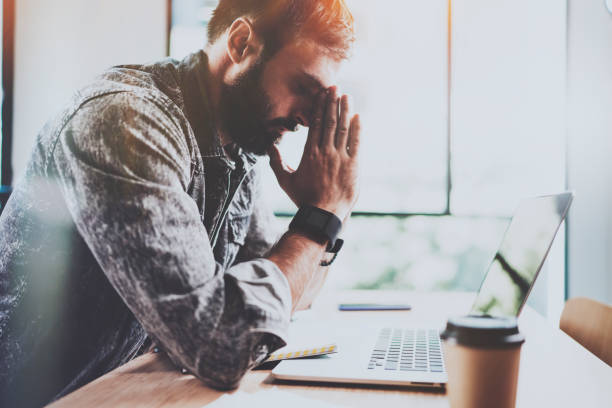 istock Coworker working process at sunny office.Tired young bearded man making pause after hard work day.Horizontal.Blurred background. 912993264