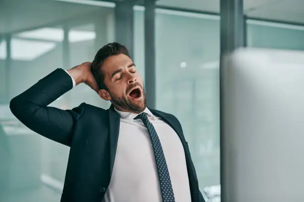 Shot of a tired young businessman stretching while  yawning with his eyes closed inside of the office