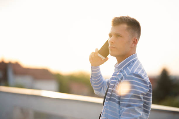 Portrait of a young, fashionable man standing at the balcony and talking on his mobile phone.
