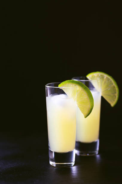 Tradtitional Italian homemade lemon and lime liqueur limoncello with ice and mint on black slate background. Alcoholic beverage. Selective focus.