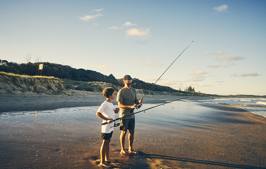 Grandfather showing his granddaughter how to fish while standing on the dock by the river.