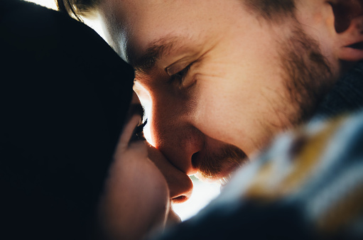 Happy girl in a hat kissing and touches noses boyfriend with a red beard and looking to his eyes. Happy moments. Close up portrait