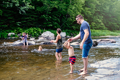 Cooling water is so welcome on hot summer days for millennials families, enjoying nature. Adults, children and family dog bathing in river. Horizontal full length shot with copy space. This was taken in Quebec, Canada.
