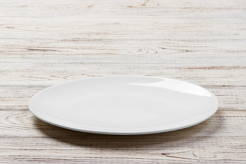 White Round Plate on white wooden table background. Perspective view.