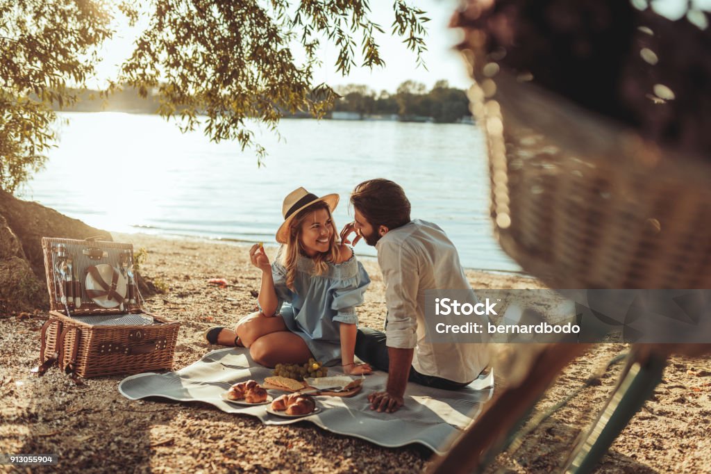 Next to you is the only place for me A young couple having a picnic at the beach Picnic Stock Photo