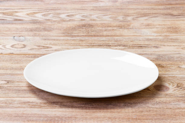 istock white plate on the wooden brown table. Perspective view 913055982