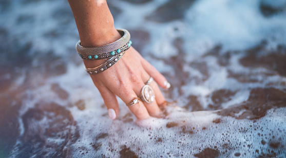 Woman with bohemian style silver rings and bracelets and her hand in the sea water