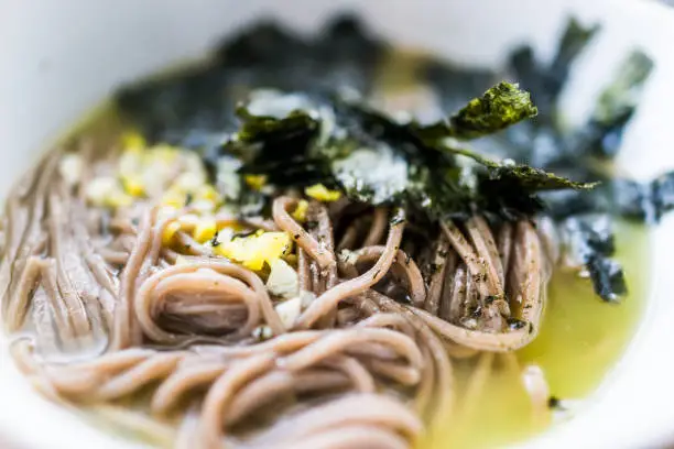 Macro closeup of soba buckwheat noodles Japanese soup with nori seaweed, ginger, green broth on hot, cold summer