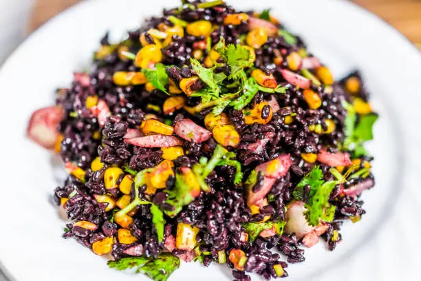 Macro closeup of forbidden Chinese black rice dish with corn, vegetables, onions, cilantro on plate isolated