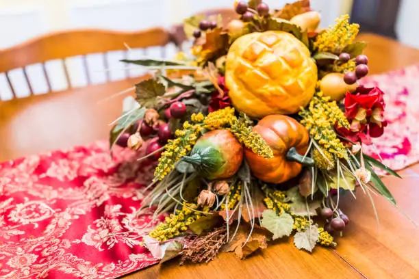 Closeup of Thanksgiving fall autumn fake cornucopia decoration on wooden table with red tablecloth in dining room