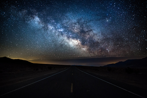 Beautiful night sky with the milky way over an empty road in Death Valley National Park. Clear sky, no lights and no People. Viewpoint from the middle of the Road. California, Southwest USA.