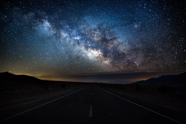 Milky Way over Country Road - Death Valley, USA Beautiful night sky with the milky way over an empty road in Death Valley National Park. Clear sky, no lights and no People. Viewpoint from the middle of the Road. California, Southwest USA. death valley national park stock pictures, royalty-free photos & images