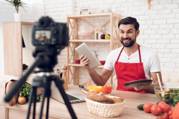 istock Chef reads from tablet for culinary podcast viewers. Vegetables and kitchen utensils. 913066082