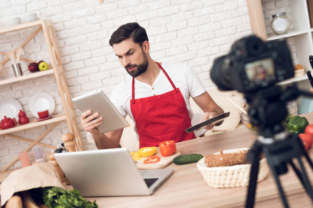 istock Chef reads from tablet for culinary podcast viewers. Vegetables and kitchen utensils. 913066084