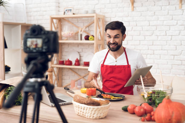 istock Chef reads from tablet for culinary podcast viewers. Vegetables and kitchen utensils. 913066110