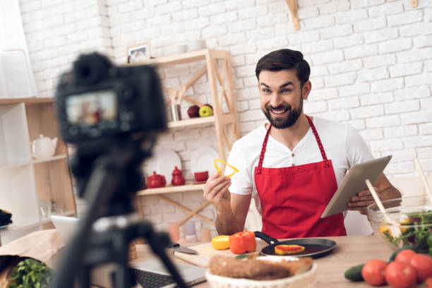 istock Chef reads from tablet for culinary podcast viewers. Vegetables and kitchen utensils. 913066120