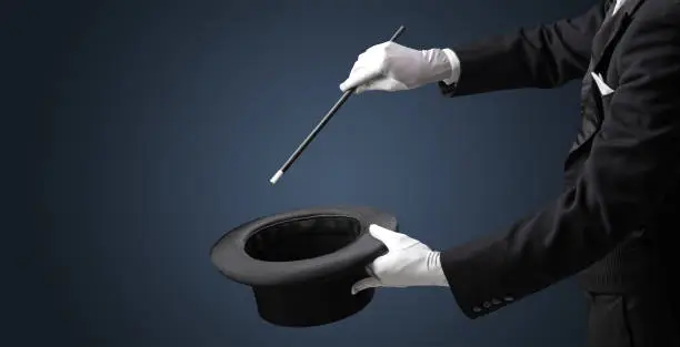 Illusionist white hand wants to conjure with magic wand from a black cylinder something