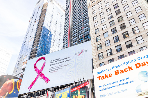New York City: Manhattan NYC buildings of midtown Times Square, Broadway avenue road, signs ads for pink ribbon breast cancer campaign, dea, national prescription drug