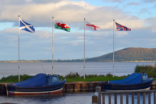 Rothesay, Scotland - 15th Juily 2023: View over part of the Marina and Esplanade of the seaside town of Rothesay on the Isle of Bute, Scotland. Pleasure craft can be seen in the marina, the Cabmen's  Rest (1874) is on the pier, a Hop-on hop-off sightseeing bus is at the bus stop, the shops and businesses of the promenade can be seen and Rothesay Castle (ruins) is in the background.