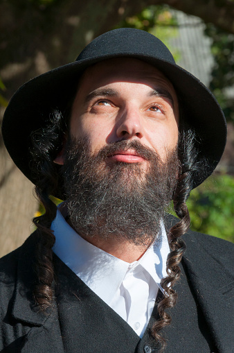 Outdoor portrait of a smiling young orthodox Hasdim Jewish man with black beard and hat