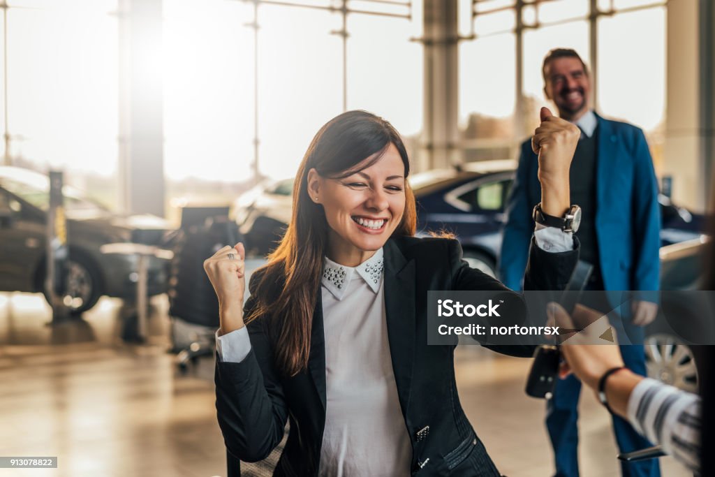 Cheerful young woman receiving the keys of her new car at car dealership. Car Stock Photo