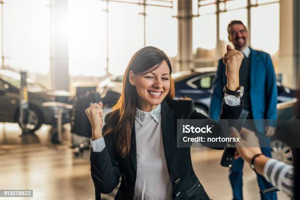 Cheerful Young Woman Receiving The Keys Of Her New Car At Car Dealership Stock Photo - Download Image Now