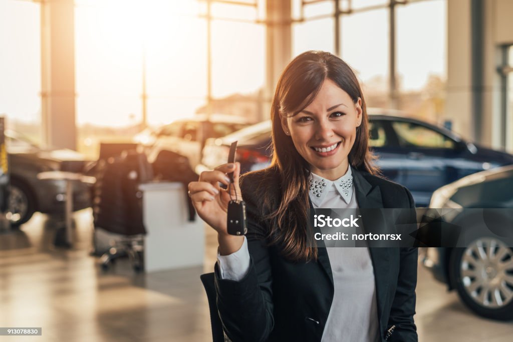 Cheerful young woman showing her new car key at dealership. Car Stock Photo