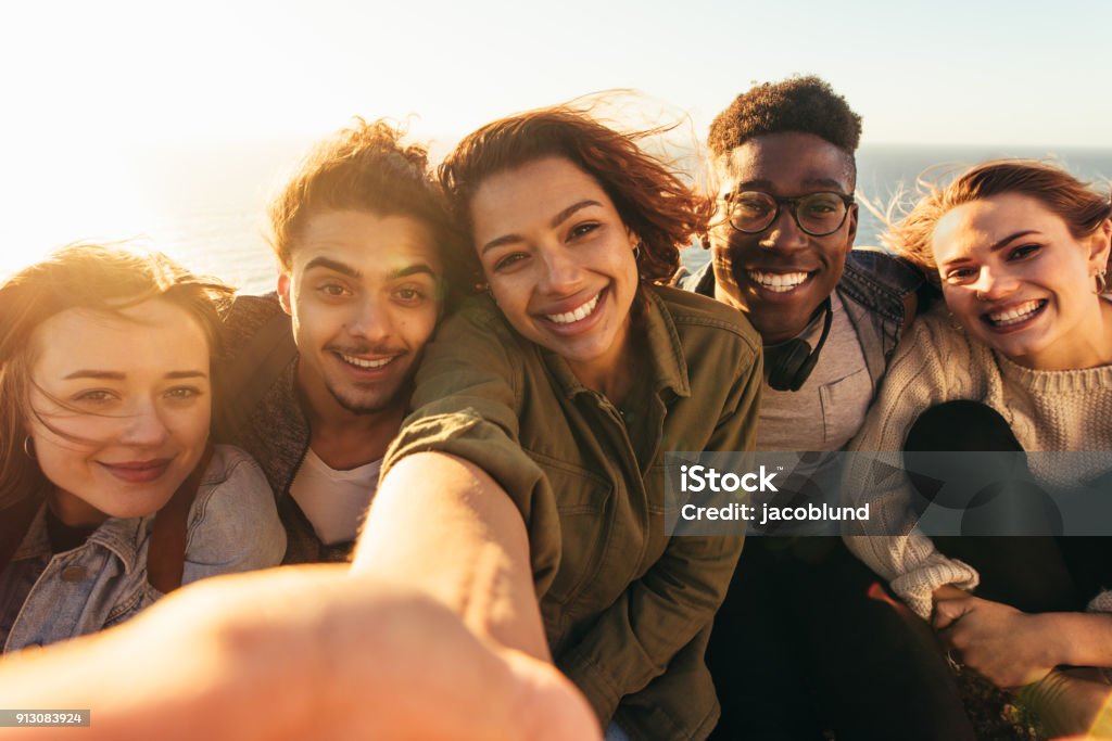 Cheerful friends taking selfie on a holiday Cheerful friends taking selfie on a holiday. Group of men and women sitting outdoors on a summer day making self portrait. Friendship Stock Photo